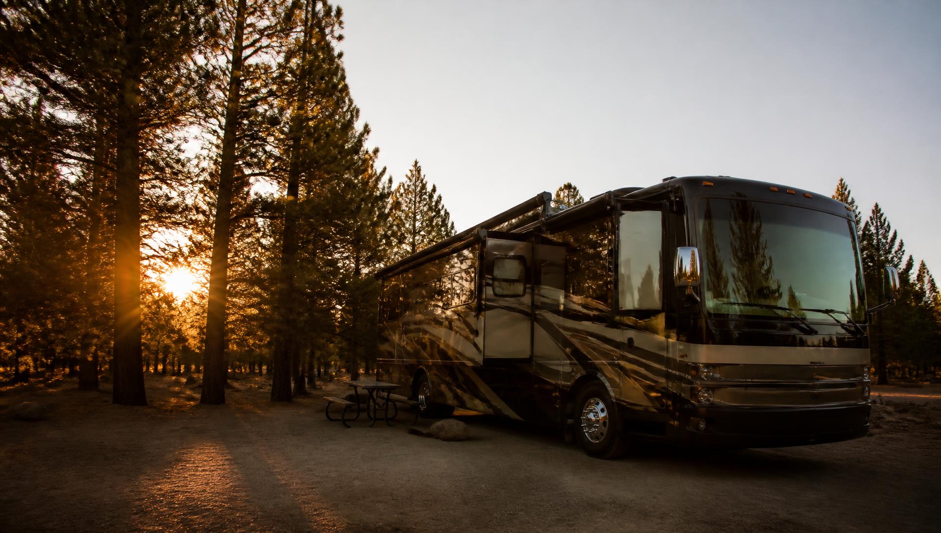 Class A motorhome parked at a wooded campground at sunset